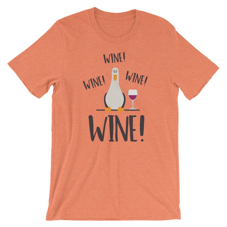 May include: A coral orange t-shirt featuring a cartoon seagull holding a glass of wine. The text "WINE!" is repeated four times on the shirt.