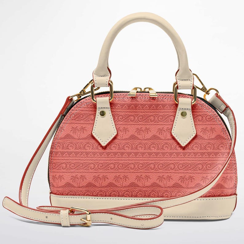 May include: A coral-colored dome handbag with a cream-colored handle and accents. The bag features a repeating pattern and a detachable shoulder strap. Gold-colored hardware adds a touch of elegance to this stylish accessory.