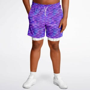Puede incluir: Pantalones cortos deportivos de color morado y azul con un patr&oacute;n de escamas de sirena. Los pantalones cortos tienen un forro interior blanco y una cintura con cord&oacute;n.