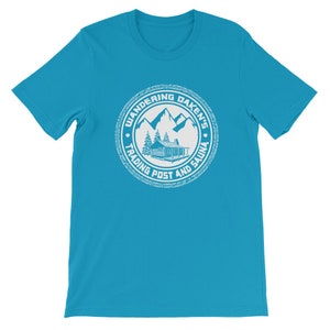 May include: A turquoise blue t-shirt with a white circular logo. The logo features a cabin in the woods with mountains in the background. The text "Wandering Daken's Trading Post and Sauna" is written around the logo.
