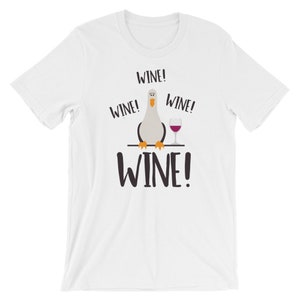 May include: White t-shirt featuring a cartoon bird holding a glass of wine. The shirt has the text "WINE!" repeated four times.