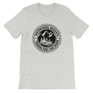 May include: A gray t-shirt with a black and white logo that says "Wandering Daken's Trading Post and Sauna". The logo features a cabin in the mountains.