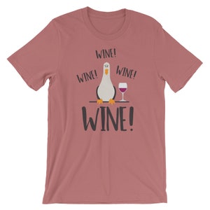May include: A pink t-shirt featuring a cartoon seagull holding a glass of wine. The shirt has the text "Wine!" repeated four times.