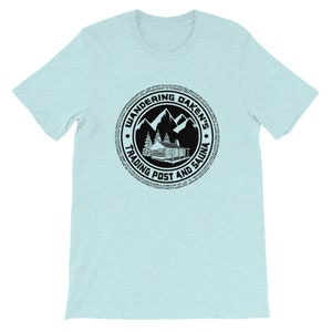 May include: A light blue t-shirt with a black circular logo. The logo features a cabin, mountains, trees, and the text "Wandering Daken's Trading Post and Sauna".