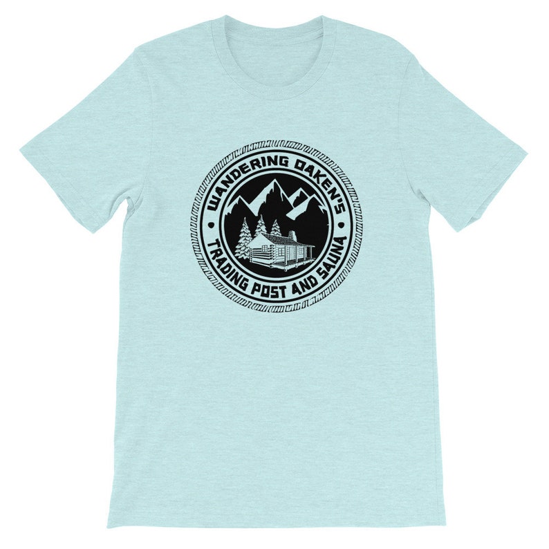 May include: A light blue t-shirt with a black circular logo. The logo features a cabin, mountains, trees, and the text "Wandering Daken's Trading Post and Sauna".