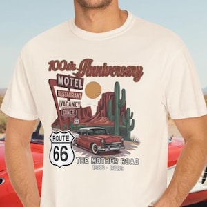 Puede incluir: Camiseta color crema con un dise&ntilde;o de la Ruta 66. El gr&aacute;fico incluye un coche antiguo, un paisaje des&eacute;rtico y el texto "100th Anniversary" y "The Mother Road 1926-2026". Tambi&eacute;n se ve un letrero de la Ruta 66.