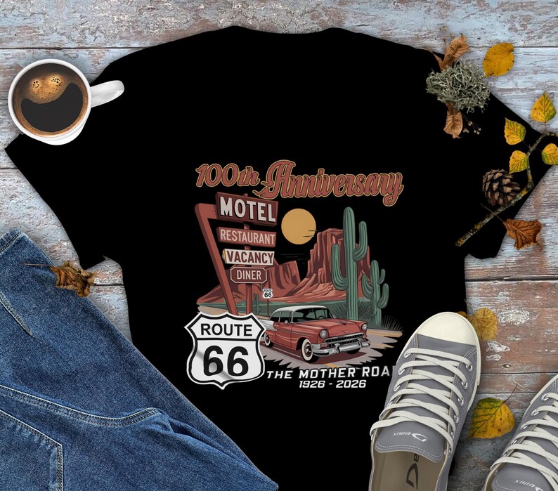 Puede incluir: Camiseta negra con un dise&ntilde;o de la Ruta 66. El gr&aacute;fico incluye un coche antiguo, un paisaje des&eacute;rtico y un letrero de motel, restaurante, habitaciones libres y restaurante. El texto dice "100th Anniversary" y "The Mother Road 1926-2026".