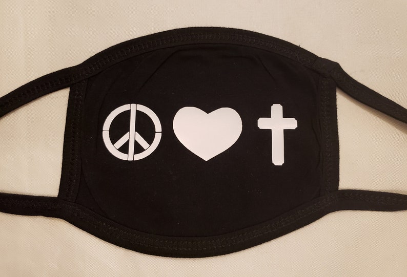 May include: Black face mask with white symbols: a peace sign, a heart, and a cross. The mask has black trim and ear loops. The symbols are printed in a bold, clean style, creating a simple yet impactful design.