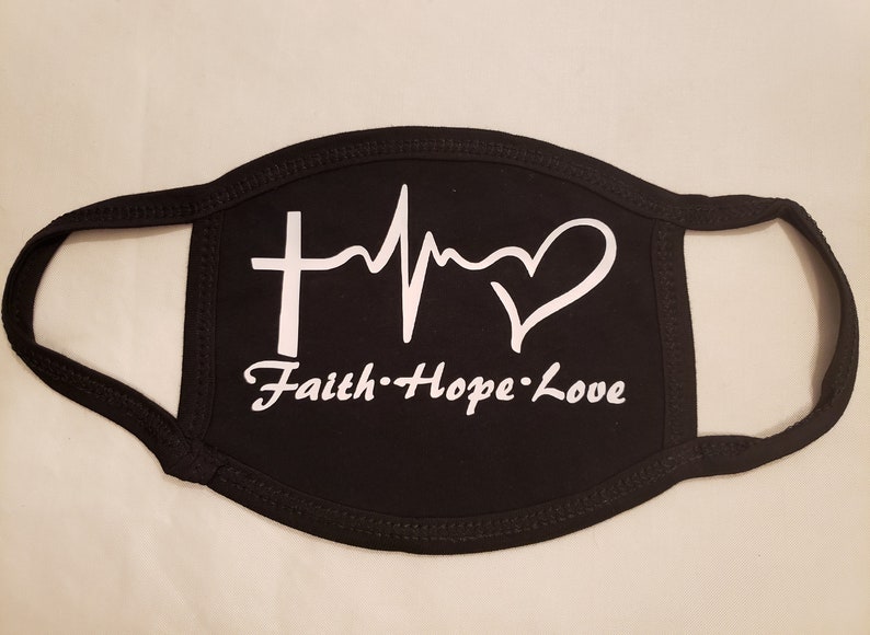 May include: Black face mask with white text and graphics. The design includes a cross, a heartbeat line, and a heart. The words "Faith Hope Love" are written below the graphics.