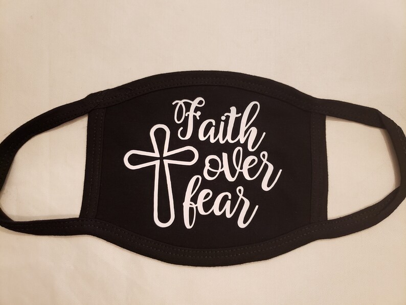 May include: Black face mask with white text and a cross design. The words "Faith over fear" are written in a cursive font. The mask has black trim and ear loops.