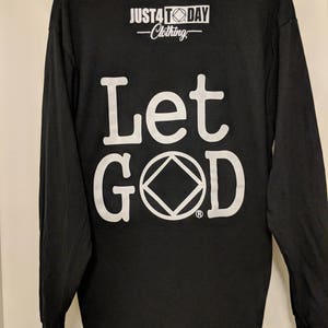 May include: Black long-sleeve t-shirt with white lettering that reads "Let God" and a white symbol. The shirt also has a small white logo that reads "Just4Today Clothing".