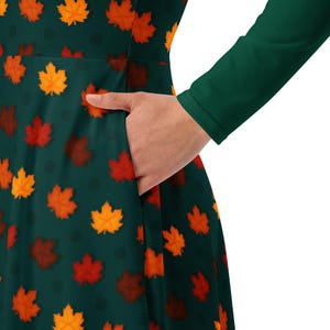May include: A green long-sleeved dress with a fall leaf print. The dress has a pocket on the left side.