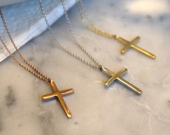 May include: Three gold cross necklaces on a white marble surface. The necklaces are different lengths and have different chain styles. The crosses are all the same size and shape.