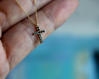 May include: A gold chain necklace with a small black diamond cross pendant.