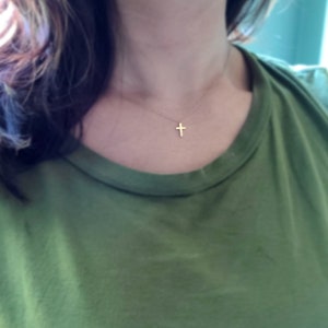 May include: A simple gold cross necklace on a person wearing a green shirt.