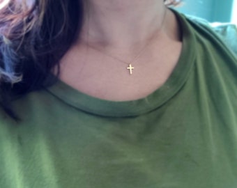 Puede incluir: Un collar sencillo de cruz dorada que lleva una persona con una camisa verde.