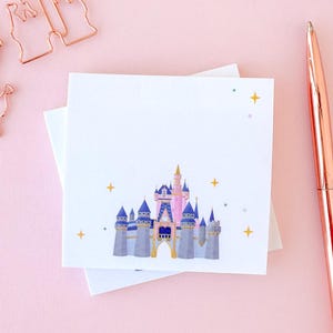 May include: White square sticky notes with a watercolor illustration of a fairytale castle in blue, pink, and gray. A rose gold pen and castle-shaped paper clips are also in the image. The pen has the word "Imagine" printed on it.