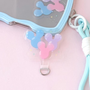 May include: A light blue phone case with a matching lanyard. The case has a wavy border and features a clear design with blue, pink, and purple Mickey Mouse-shaped balloons. The lanyard is light blue and white.