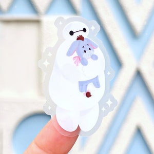 May include: A white, cartoon-style robot with a red heart on its chest, holding a small, blue, cartoon-style pig in its arms. The robot and pig are on a clear sticker with a sparkly background.