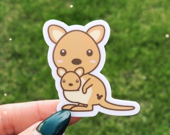 May include: A brown and tan cartoon kangaroo sticker with a smaller kangaroo joey in its pouch. The kangaroo has a small black Mickey Mouse-shaped design on its back.