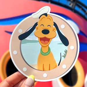 May include: A circular Pluto sticker featuring the Disney character Pluto with a happy expression, wearing a sailor hat and green collar. The sticker has a light brown border with white dots and a background of a beach scene.