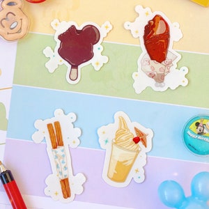 May include: A collection of colorful stickers featuring Disney-themed treats, including a Mickey Mouse-shaped ice cream bar, a turkey leg, churros, and a soft-serve ice cream. Other items include a "1st Visit" pin, a Mickey Mouse-shaped pin, and a "Happy Birthday" pin.