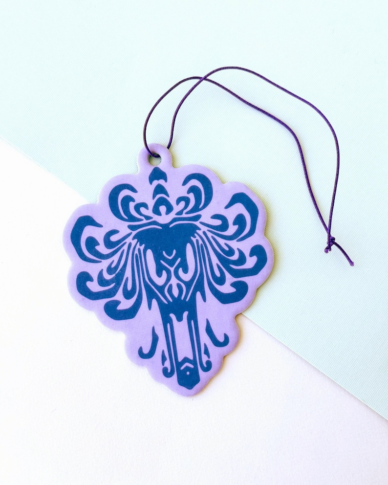 May include: Purple car air freshener with a dark blue Haunted Mansion logo. The logo is a stylised ghost face with a crown and a swirling design.