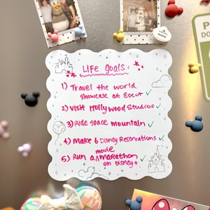 以下が含まれることがあります： ディズニーをテーマにしたマグネットと、手書きの「Life Goals」リストで飾られた冷蔵庫。リストには、ハリウッドスタジオを訪れたり、マラソンをしたりするなどの目標が含まれています。ミニーマウスの耳のカチューシャと写真も表示されています。