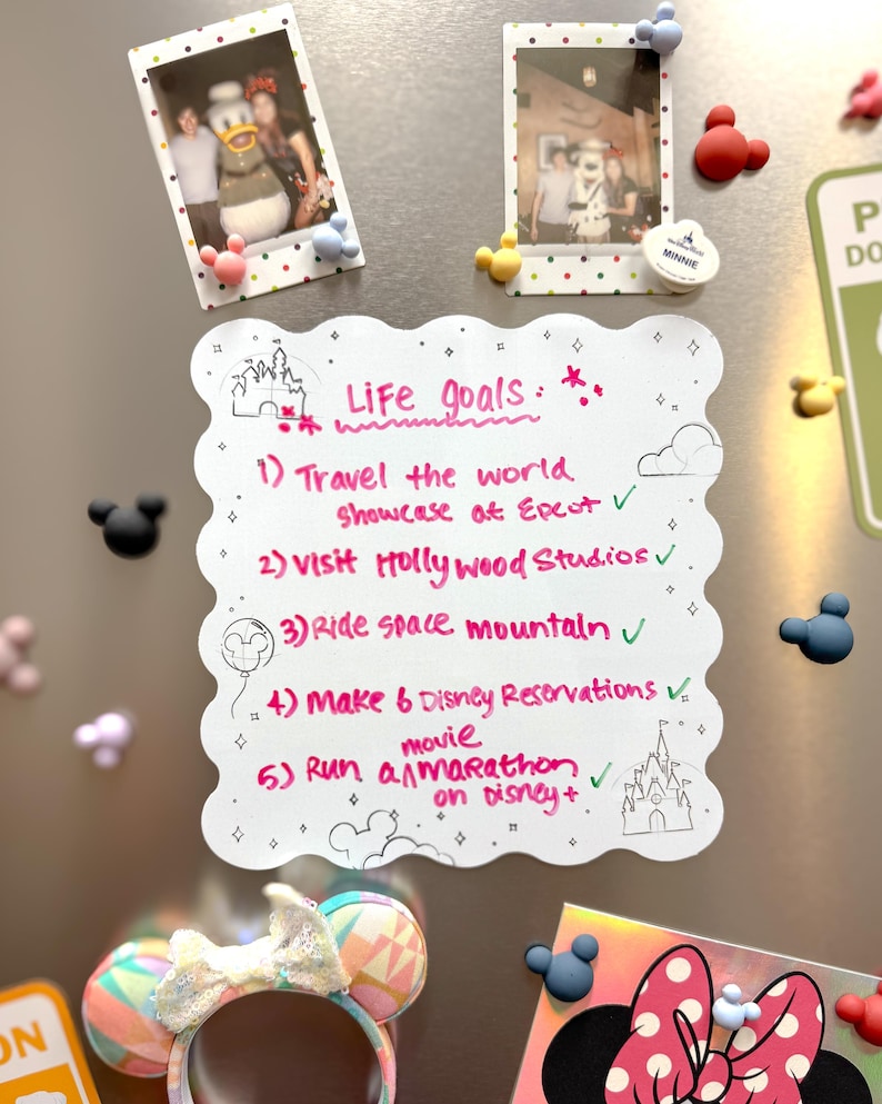 以下が含まれることがあります： ディズニーをテーマにしたマグネットと、手書きの「Life Goals」リストで飾られた冷蔵庫。リストには、ハリウッドスタジオを訪れたり、マラソンをしたりするなどの目標が含まれています。ミニーマウスの耳のカチューシャと写真も表示されています。