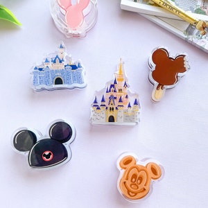May include: A selection of clear acrylic pins with Disney-themed designs. Includes a pink Minnie Mouse, two castle designs, a Mickey Mouse ice cream bar, a black Mickey Mouse, and a Mickey Mouse waffle.