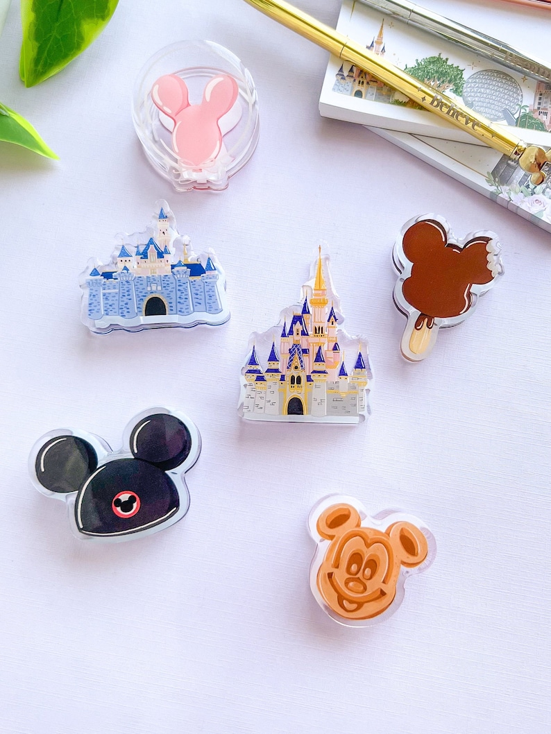 May include: A selection of clear acrylic pins with Disney-themed designs. Includes a pink Minnie Mouse, two castle designs, a Mickey Mouse ice cream bar, a black Mickey Mouse, and a Mickey Mouse waffle.