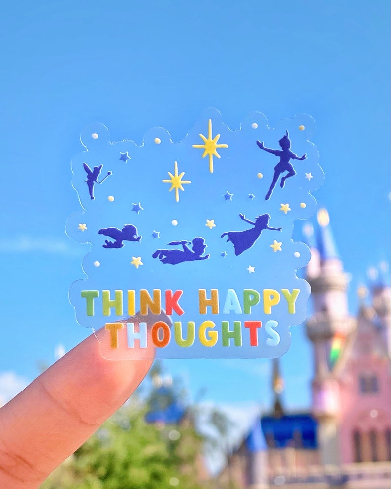 Op de afbeelding: Een transparante sticker met een blauw, geel en wit ontwerp met silhouetten van personages uit de film Peter Pan. De sticker heeft de tekst "Think Happy Thoughts" in regenboogkleuren.