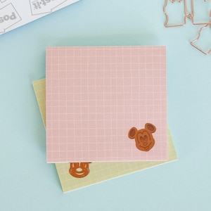 May include: A square pink sticky note with a white grid pattern and a brown Mickey Mouse head icon in the bottom right corner, layered over a light green grid sticky note that shows a partial brown Mickey Mouse head icon at the bottom.