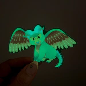 Peut inclure: Un autocollant vert qui brille dans le noir repr&eacute;sentant une cr&eacute;ature ail&eacute;e avec des ailes brunes et vertes. La cr&eacute;ature a une t&ecirc;te bleu clair et un visage jaune.