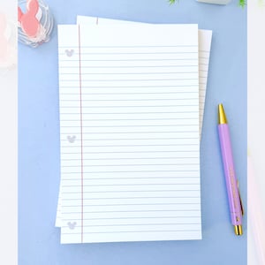 May include: White lined paper with a red margin line and Mickey Mouse head accents. A purple pen with gold accents lies next to the paper. The background is a light blue surface.