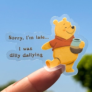 May include: A transparent sticker featuring a smiling yellow bear wearing a red shirt and holding a honey pot. The sticker has the text "Sorry, I'm late... I was dilly dallying" in a light blue bubble.