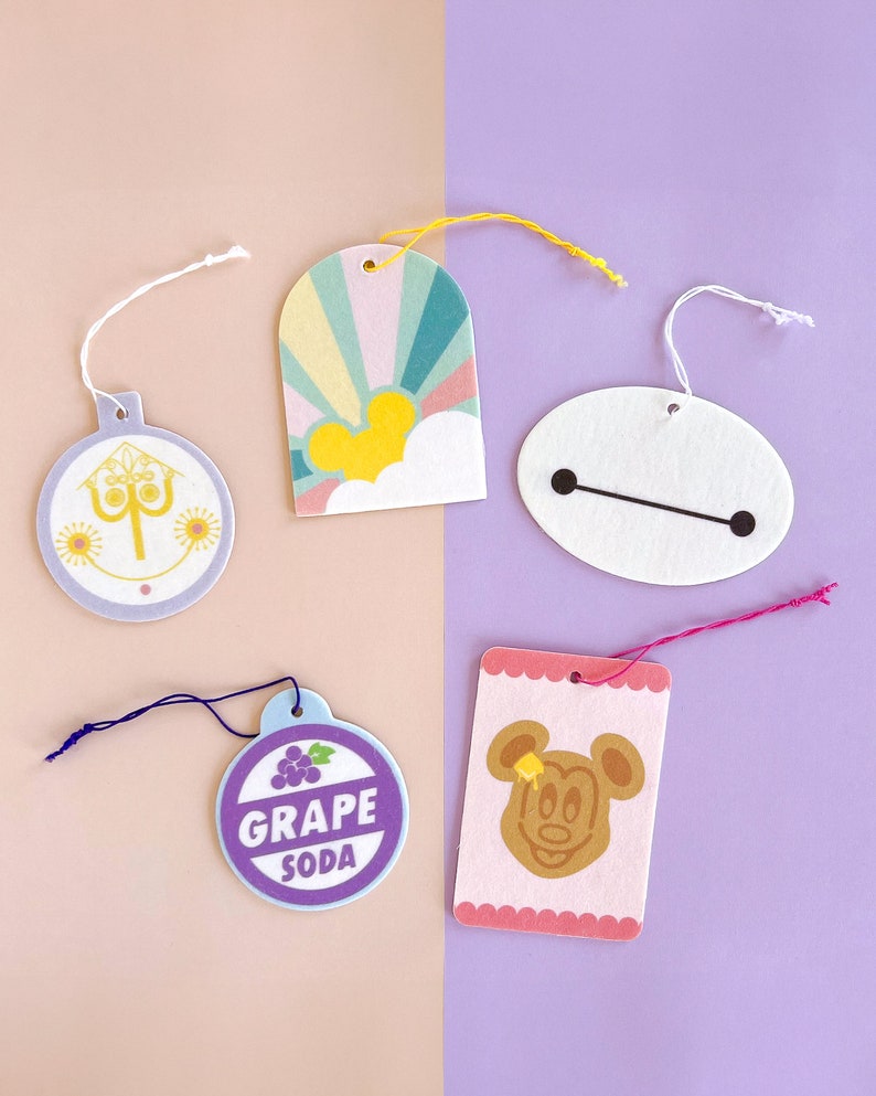 May include: Five colourful paper tags with string attached. The tags feature various Disney characters and designs, including Mickey Mouse, Baymax, a grape soda logo, and a design with a castle and fireworks.