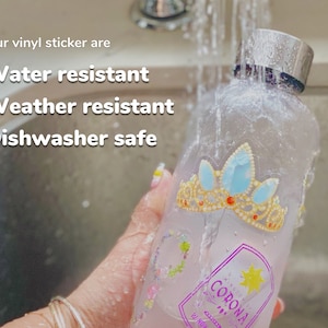 Puede incluir: Una botella de vidrio transparente con una tapa plateada y una pegatina colorida con una corona y el texto "Corona" se est&aacute; enjuagando bajo el agua corriente. El texto "Our vinyl sticker are Water resistant Weather resistant Dishwasher safe" es visible en la parte superior de la imagen.