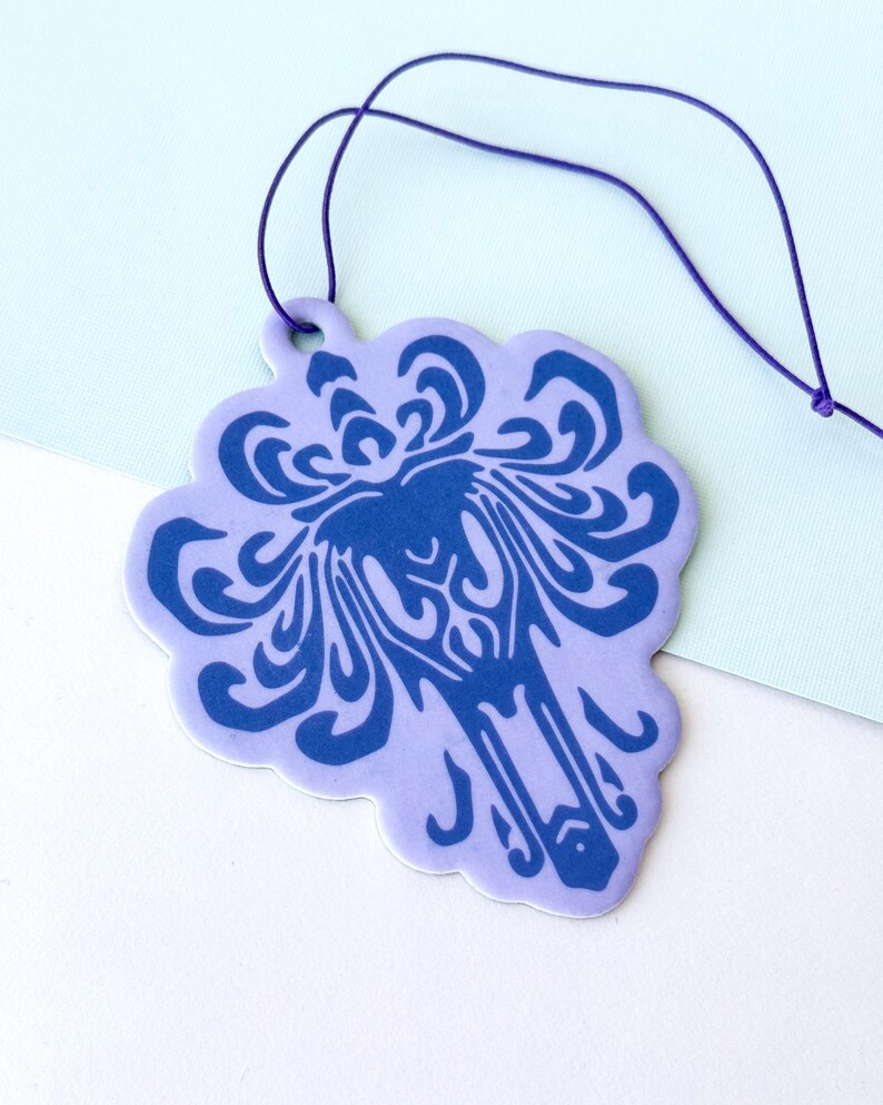 May include: A purple car air freshener with a blue floral design. The air freshener is hanging from a purple string.