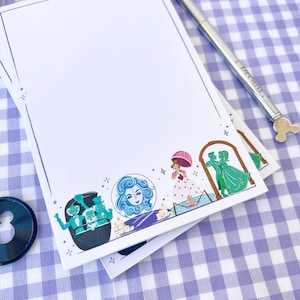 Puede incluir: Una pila de blocs de notas blancos sobre un fondo a cuadros azules y blancos. El bloc de notas superior tiene un borde azul e ilustraciones de personajes de la Mansi&oacute;n Encantada de Disney y un bol&iacute;grafo plateado.