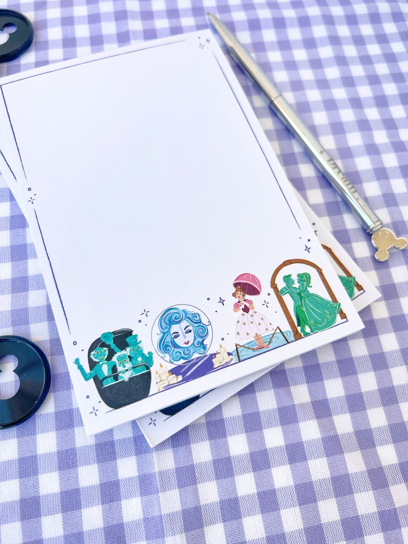 Puede incluir: Una pila de blocs de notas blancos sobre un fondo a cuadros azules y blancos. El bloc de notas superior tiene un borde azul e ilustraciones de personajes de la Mansi&oacute;n Encantada de Disney y un bol&iacute;grafo plateado.