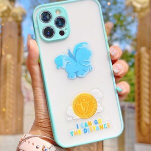 Puede incluir: Funda transparente para tel&eacute;fono con borde y detalles de c&aacute;mara en azul claro. La funda presenta un Pegaso de dibujos animados azul y un gr&aacute;fico de moneda de oro con el texto "I CAN GO THE DISTANCE".