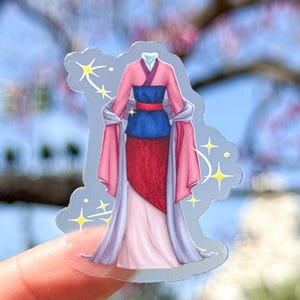 May include: A clear sticker featuring a cartoon illustration of a pink, blue, and red dress with a long, flowing purple and pink robe. The dress has a blue sash and a red skirt. The sticker is surrounded by small, sparkling stars.