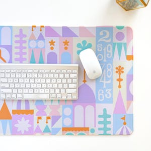 May include: A pastel-coloured mouse mat with a whimsical design of geometric shapes, numbers, and floral elements. A white keyboard and mouse are on the mat. The design includes the numbers 2, 5, 19, 78, 4, and 63.