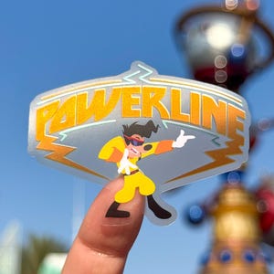 May include: A transparent sticker with the word "POWERLINE" in yellow and orange. It features a cartoon character in a yellow outfit, sunglasses, and a white glove, in a pose. The background is a blurred blue sky.