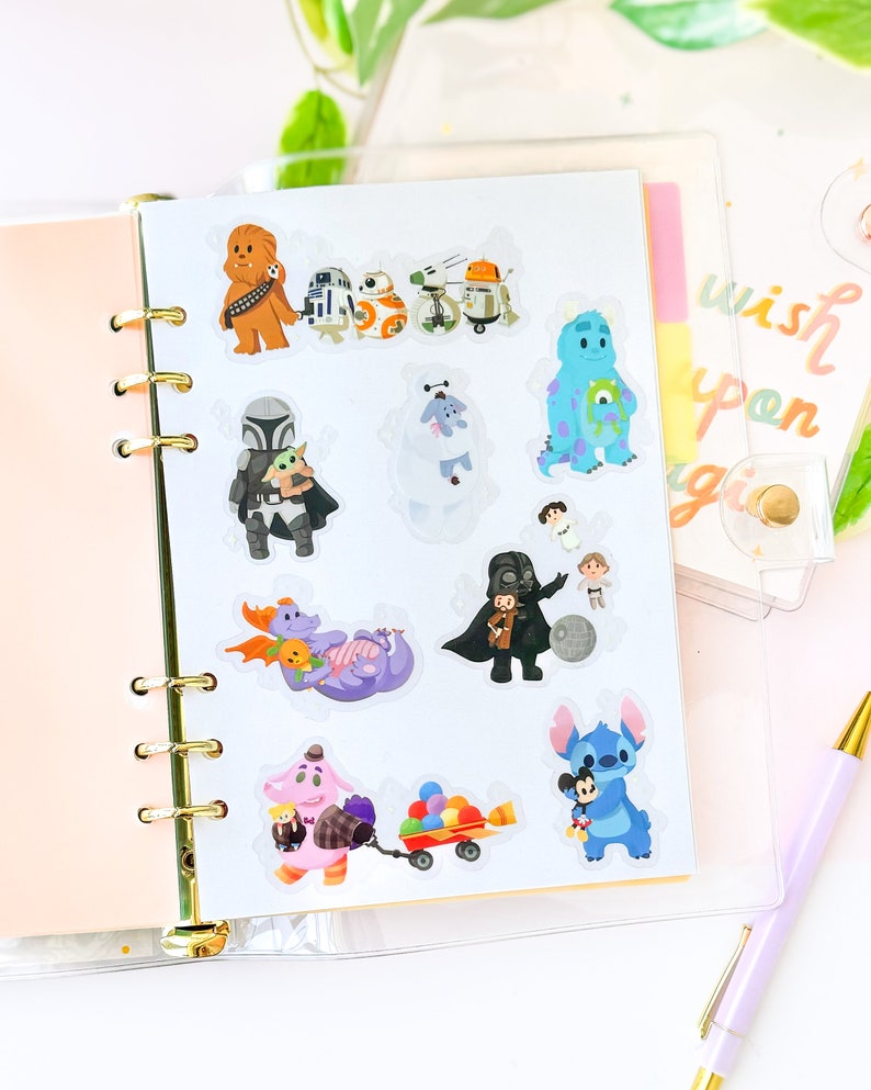 May include: A sheet of clear stickers featuring various Disney and Star Wars characters. The stickers include Chewbacca, R2-D2, BB-8, a droid, a blue monster, a Mandalorian with Grogu, a white furry creature, Darth Vader with a Stormtrooper, a purple dragon, a purple monster with a hat, a red wagon with colorful balls, and Stitch holding Mickey Mouse.