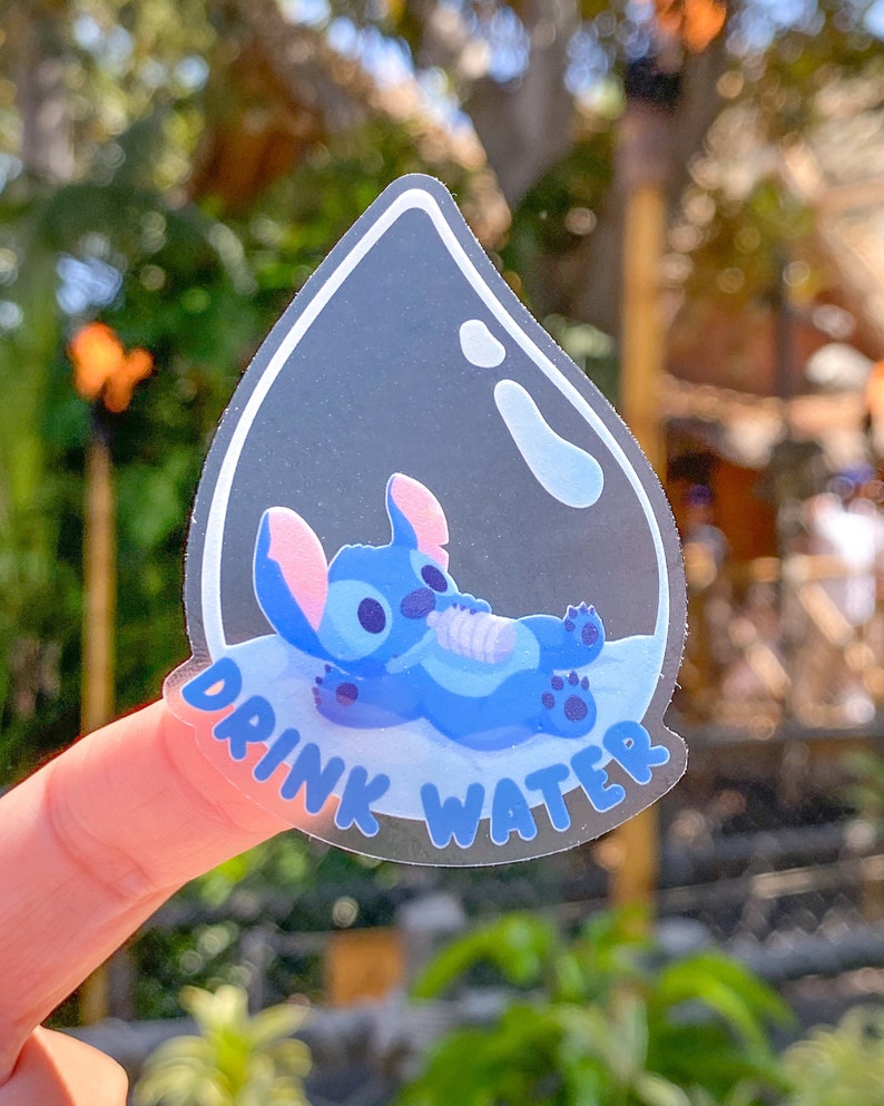 May include: A clear water drop sticker featuring a blue Stitch character from Lilo & Stitch lying inside. The sticker reads "Drink Water" in black lettering.