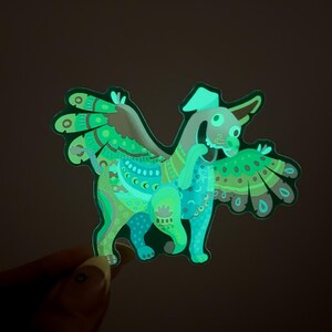 May include: A green and blue glow-in-the-dark sticker of a fantastical creature with wings, a hat, and intricate patterns.