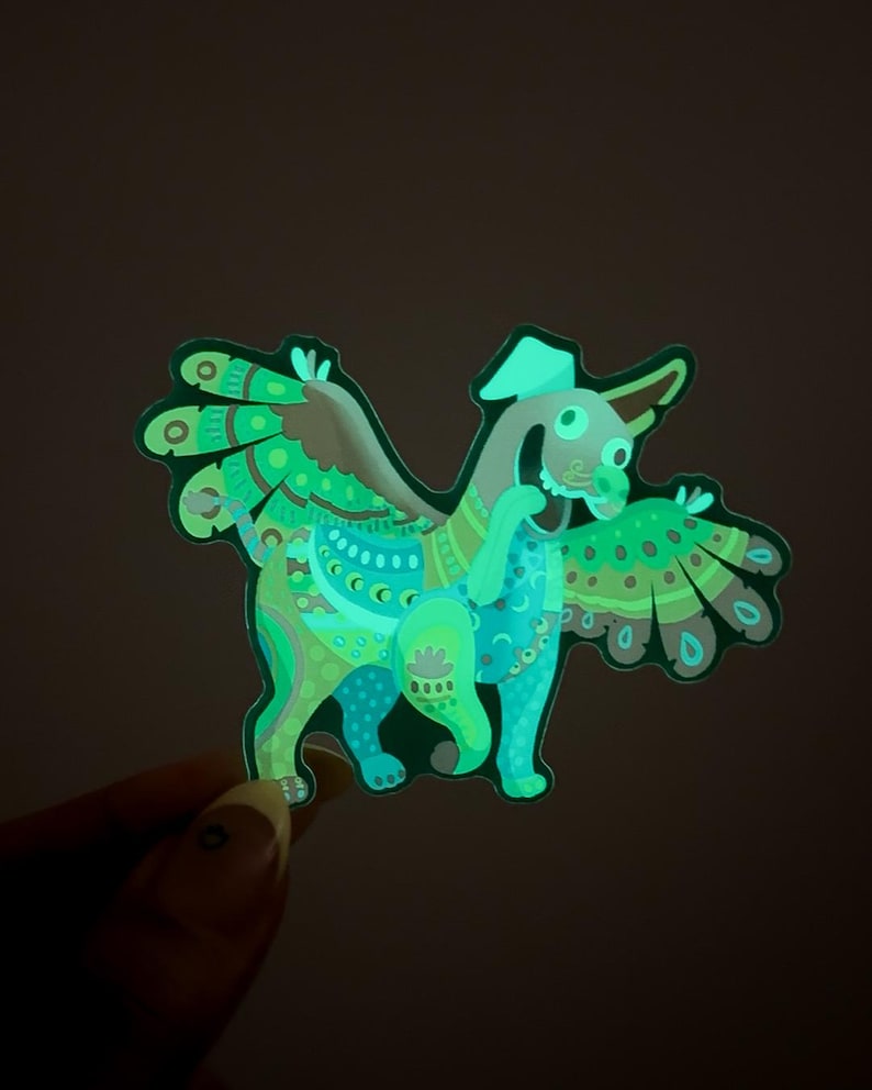 May include: A green and blue glow-in-the-dark sticker of a fantastical creature with wings, a hat, and intricate patterns.