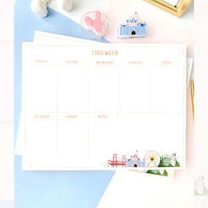 Peut inclure: Un planificateur hebdomadaire blanc avec des accents dorés et un thème Disney. Le planificateur a des espaces pour chaque jour de la semaine, y compris le samedi et le dimanche, et une section notes. Le bas du planificateur présente une illustration colorée de monuments Disney, notamment le château, une grande roue et un pont.